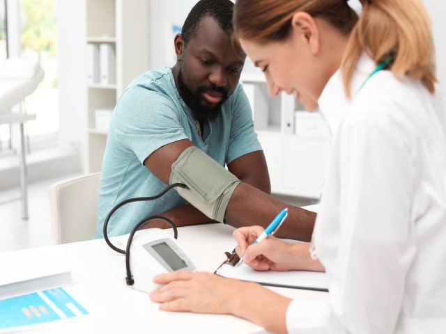 Patient bei einer Blutdruckmessung in einer Arpraxis mit Fokus auf das Messgerät.