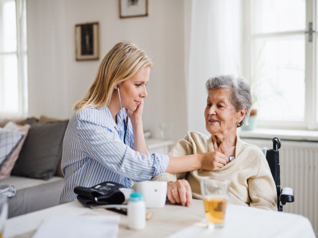 Pflegekraft unterstützt ältere Frau in einem hellen Wohnzimmer.