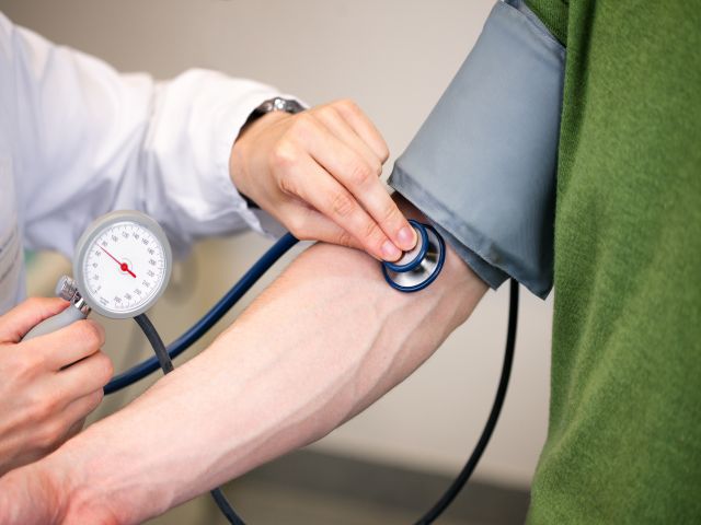 Blutdruckmessung mit einem Stethoskop und Blutdruckmessgerät am Arm eines Patienten.