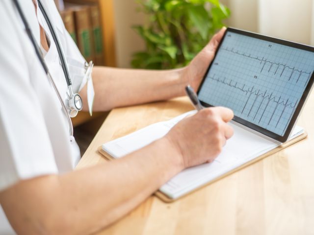 Arzt analysiert ein EKG auf einem Tablet und macht Notizen.