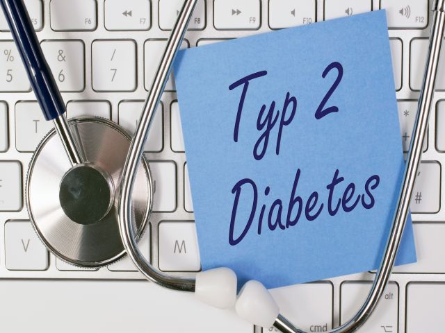 Blauer Zettel mit der Aufschrift "Typ 2 Diabetes" auf einer Tastatur, daneben ein Stethoskop.