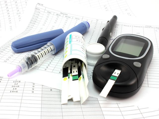 Blutzuckermessgerät mit Teststreifen, Insulinspritze und Pen auf Tabellen zur Diabetesüberwachung